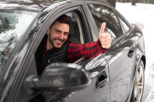 Young attractive Caucasian man sits at the wheel of his car sunny winter day. photo