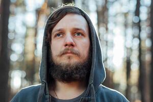 close up portrait of a bearded hipster tourist in gray hood man in the sunlight woods forest photo