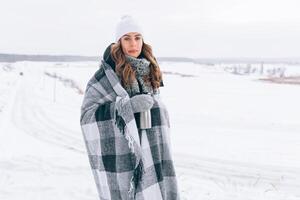 beautiful girl in winter covered with a plaid with a thermos mug and hot tea photo