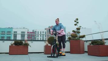 saudável caucasiano mulher exercício exercite-se em estacionário ciclismo máquina bicicleta em casa telhado Academia video