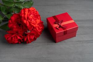 Beautiful red roses next to a gift red box on a dark cement background. photo