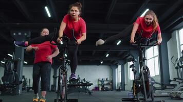 grupo atlético muchachas ejecutando aerobio montando formación ejercicios en ciclismo estacionario bicicleta en gimnasio video