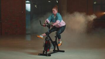 Healthy Caucasian woman exercising workout on stationary cycling machine bike in gym, Slow Motion video