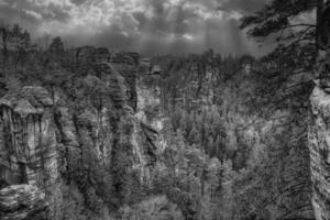 Jagged rocks on the Basteibridge in black and white. View over trees and mountains photo