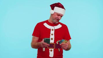 Mens in Kerstmis t-shirt gebruik makend van credit bank kaart, smartphone terwijl overbrengen geld boodschappen doen online video