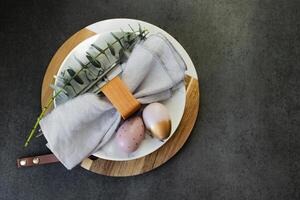 Happy Easter holiday concept. Flat lay photo of marble plate, easter eggs, cutlery and branches of eucalyptus on dark background table.