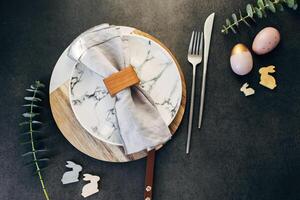 Easter table setting concept. Plate, easter eggs, cutlery and branches of eucalyptus on dark background table. Flat lay, top view photo