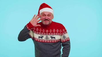 Positive man in Christmas sweater with deers waves hand palm in hello gesture welcomes someone video