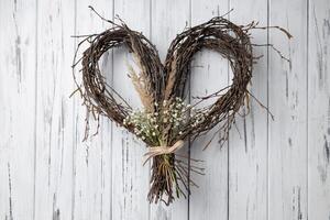 Wicker heart shaped wreath of birch branches hanging on aged wooden wall photo