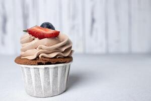 Chocolate cupcake with cream cheese frosting, strawberry and blueberry on light background photo