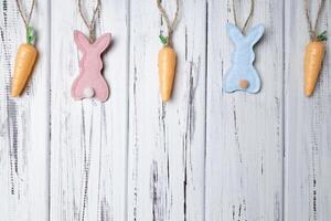 Carrots, pink and blue bunnies on white vintage aged wooden background. Copy space photo