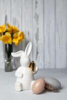 Easter bunny and eggs on table, bouquet of daffodils on background. Copy space photo