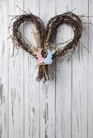 Wicker heart shaped wreath of birch branches with bunnies on it hanging on white aged wooden wall photo