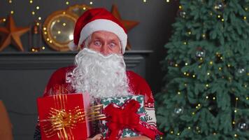 Senior grandfather parodies Santa Claus presenting Christmas gift box, holidays celebration at home video