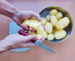 Close up of man holding and peeling potato. Hands cutting potatoes at kitchen to prepare a recipe. photo
