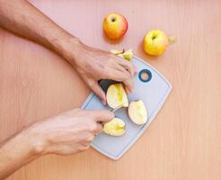 Close up male hands cut an apple into slices. Top view of preparing fruits over kitchen table. photo