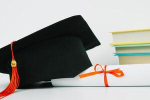 A black square graduate hat with a red tassel lies on a diploma and a stack of books. Education concept photo