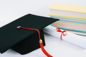 A black square graduate hat with a red tassel lies on a diploma and a stack of books. Education concept photo