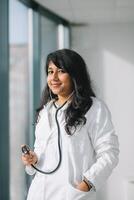 indio mujer médico o enfermero a el clínica en práctica. hembra médico en un blanco Saco con un estetoscopio foto