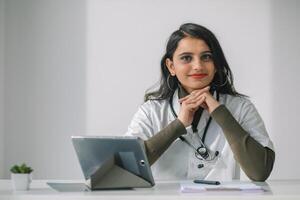 Indian female doctor in a white coat with a stethoscope conducts an online consultation in her office photo