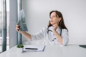 Young caucasian woman doctor wearing white medical coat and stethoscope holds the x-ray photo