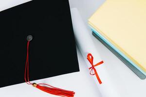 un negro cuadrado graduado sombrero con un rojo borla mentiras en un diploma y un apilar de libros. educación concepto foto