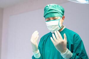 Male surgeon wearing medical protective gloves and surgical mask in operation theater at hospital, Medical team performing surgical operation in operating room photo
