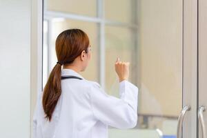 Back view of Young female doctor knocking on door photo