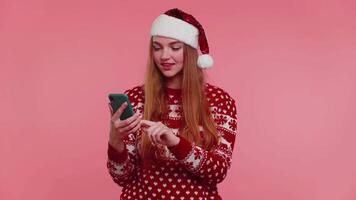 vrouw in Kerstmis trui op zoek smartphone Scherm vriendelijke groet verheugt winnen succes geluk, duim omhoog video