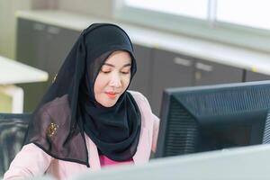 Young Muslim businesswoman in an office, young Arabic woman in a headscarf using a pc computer photo