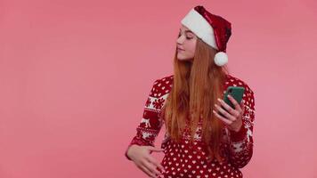 Girl in Christmas Santa sweater with mobile phone showing pointing empty place, advertising area video