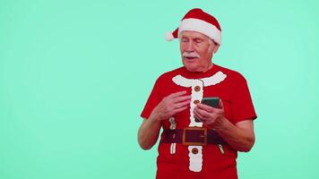 abuelo Papa Noel Navidad camiseta con móvil teléfono demostración señalando vacío lugar, publicidad zona video