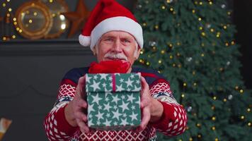 Senior grandfather in New Year sweater and hat presenting Christmas gift box, holidays at home video