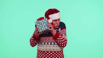 Senior grandfather man in Christmas sweater received present, interested in what inside gift box video