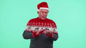 Rico mayor hombre ganador en Navidad rojo suéter demostración debilitante, lanzamiento dinero alrededor, compras video