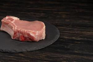 Top view of one pieces raw pork chop steaks on a black stone cutting board. photo