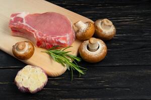 Top view of one pieces raw pork chop steaks with rosemary Champignon mushrooms and garlic on a cutting board. photo