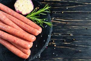 Juicy sausages for barbecue lie on a stone chopping board with rosemary and spices, pepper and coarse salt photo