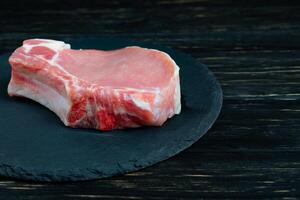 Top view of one pieces raw pork chop steaks on a black stone cutting board. photo