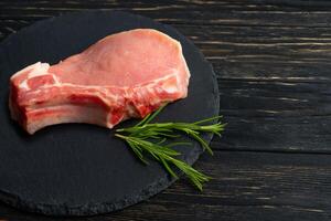 Top view of one pieces raw pork chop steaks with rosemary on a black stone cutting board. photo