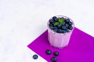 Tasty fresh blueberry yoghurt shake dessert in glass standing on white table purple napkin background. photo