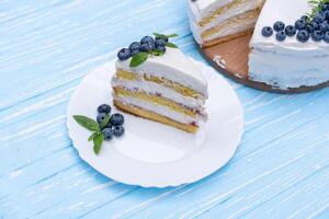 Appetizing cheesecake cake biscuit pillow decorated white cream blueberries and mint stands on wooden blue rustic table photo