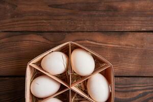 White chicken eggs lie in round wooden basket which stands on a dark wooden table. photo