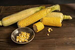 Corn cob with green leaves lies on table Dark wooden background. photo