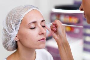 Cosmetology cabinet client sitting on couch. Beautician applies marking on eyebrows. photo