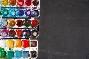 Set of watercolor paints on a black background. Brushes drawing. Creative background. School for teaching drawing. photo