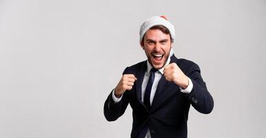 Young handsome caucasian guy in business suit and Santa hats stands on white background in studio screams and fights hold fists for sparring photo