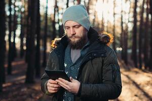Portrait of adult man walking in the pine forest with digital tablet. photo