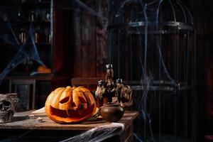 Halloween. Scary Halloween pumpkin with carved face on table in dark room with candles, spider web, and cage on background photo