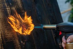 profesional carpintero utilizando antiguo tradicional japonés técnica. ardiente madera tablones con gas quemador foto